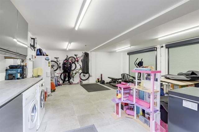 A peek inside the double garage reveals that there is space and plumbing for a washing machine, as well as space for a tumble dryer. It also includes a range of fitted base and wall units with a worktop, tiled flooring and ceiling strip lights.