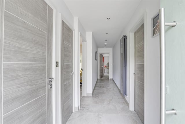 The long entrance hallway that links most of the rooms in the £750,000 bungalow. It has tiled flooring, recessed spotlights, an in-built cloak cupboard, vertical radiator and a wall-mounted security alarm.