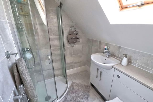 Here is the excellent en suite shower room to one of the bedrooms upstairs. A two-piece white suite consists of a shower cubicle and wash basin with storage unit. The floor and walls are tiled, while the Velux window faces the front of the house.