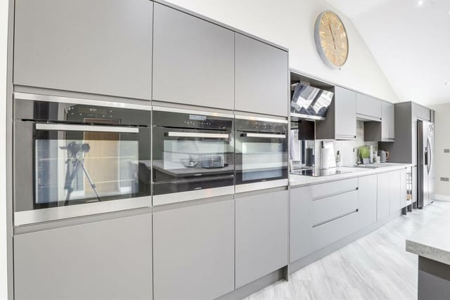 The kitchen is equipped with three integrated ovens and an integrated hob with an extractor hood above.