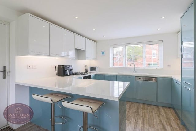 The dining kitchen is fitted with a range of modern, matching high-gloss wall and base units, with work surfaces, an inset ceramic sink, a breakfast bar and ceiling spotlights. Integrated appliances include an electric oven, gas hob, fridge freezer and dishwasher