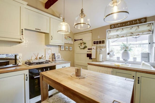 The kitchen features a range of fitted base and wall units, with wood-effect worktops, a ceramic sink-and-a-half with mixer tap and drainer, and a self-adhesive blackboard wall. A tiled floor, an exposed beam to the ceiling and a single wooden door to the back garden add to its appeal.