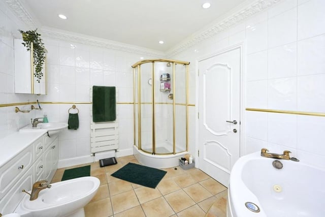 A sparkling bathroom that is fitted with a white suite comprising corner spa bath, separate shower cubicle, low-level WC with bidet, two wash hand basins with vanity storage under, heated towel-rails and tiled walls and floor.