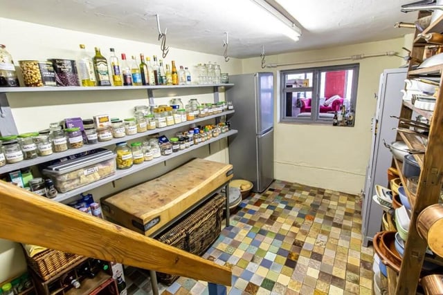 Steps in the kitchen lead down to this walk-in pantry, with its multi-coloured, tiled floor. It includes extensive shelving, ceiling hooks and a window looking through to the main living room.